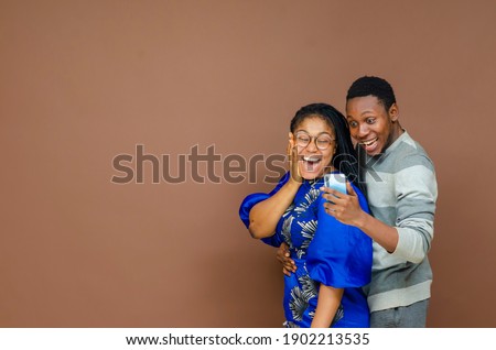 mix race couple have fun together standing close to a brown background concentrated at smart phone screen