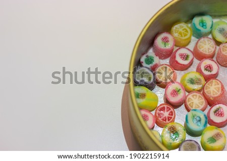 Multicolored lollipops in different flavors in a tin can on a white table, space for text. Candy sweets with drawing of fruits for children