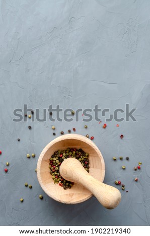 Multi-colored red green black peppercorns in a wooden mortar with pestle and scattered around on a ultimate gray concrete background close-up with a place for text. seasoning. ingredients.
