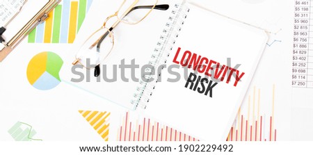 Text LONGEVITY RISK on white notepad, glasses, graphs and diagrams.