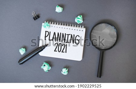 Paper notepad with text Planning 2021, crumpled papers sheets and magnifier glass on dark background