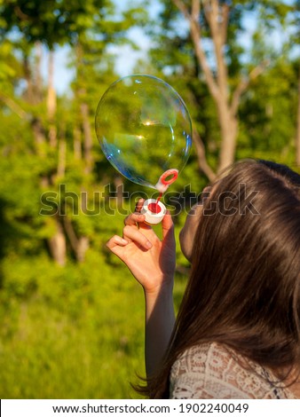young girl inflates soap bubbles in summer in sunny weather, outdoor recreation, big soap bubbles