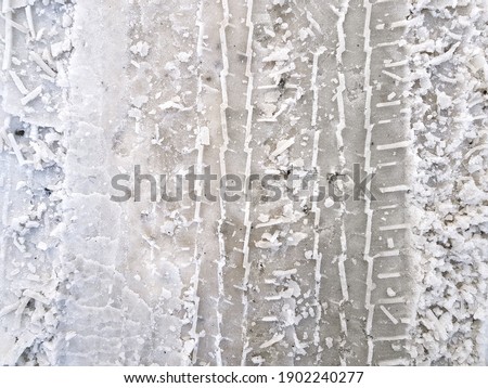 Tires prints of the cars wheels on road surface covered with dirty white melting snow. Abstract winter vertical lines background.