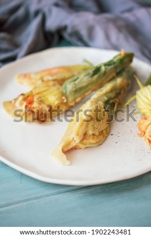 Battered and deep fried Courgette or Zucchini squash blossoms shot from above over a blue rustic table with blurred foreground and background.
