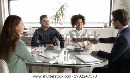 Happy diverse business partners shaking hands at meeting in modern boardroom, group negotiations, African American businesswoman and businessman making agreement, great deal, signing contract