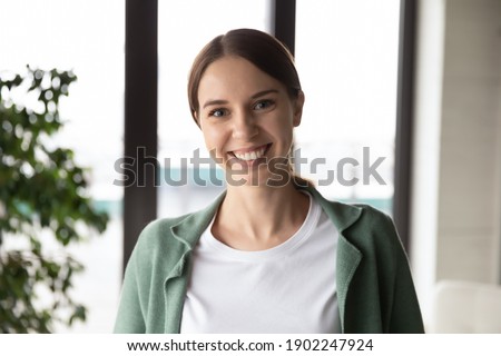 Head shot portrait smiling businesswoman successful confident executive ceo looking at camera, standing in modern office with panoramic windows, young beautiful employee intern posing for photo