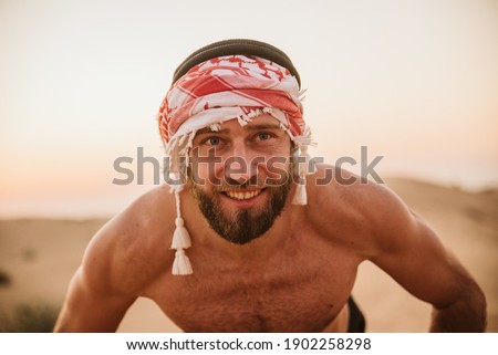 A portrait of a smiling bearded guy doing push-ups in the desert