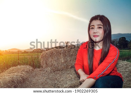 A young Asian woman in a red blouse sits on the straw in the morning sun.