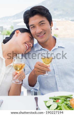 Happy couple having white wine with a meal outside on a balcony