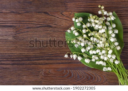 Bouquet of lilies of the valley on a brown wooden background. Vintage retro flowers as background for business text. Spring and summer decoration for women. Composition of field flowers of lilies.