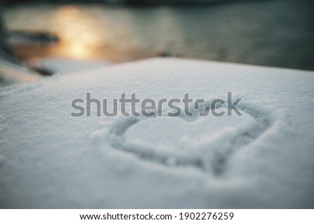 A heart symbol painted on fresh white snow against a sunset background