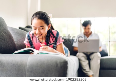School kid little girl learning and looking at book making homework studying knowledge with online education e-learning system.children video conference with teacher tutor at home