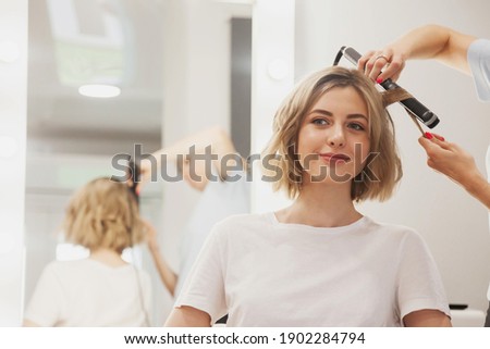 Hairdresser does hairstyle cute pretty young woman in beauty salon. Customer service in interior room create an amazing image. Work hairstyles creation wizard. Concept style, satisfaction. Copy space Royalty-Free Stock Photo #1902284794