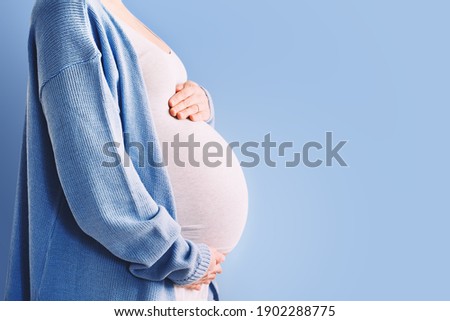 Beautiful pregnant woman hugging her belly in white background. Expectant mother waiting for baby birth during pregnancy. Concept of maternal health, visiting doctor and gynecological checkup. Royalty-Free Stock Photo #1902288775