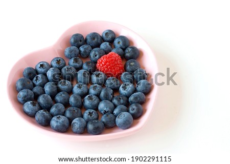 Bunch of blueberries and one raspberry on the heart shaped pink plate. Health concept.