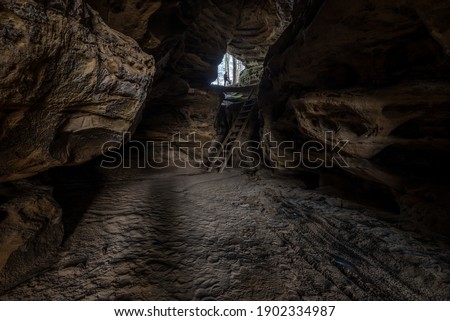 Dark cave feature with sandy floor, ladder and lone female explorer 