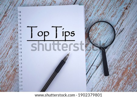 Selective focus image of magnifying glass with a pen on a wooden background with Top Tips wording . Vintage style. Business and economy concept.