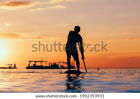 Active paddle boarder. Black sunset silhouette of young sportsman paddling on stand up paddleboard. Healthy lifestyle. Water sport, SUP surfing tour in adventure camp on family summer beach vacation.