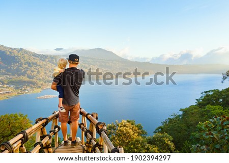 Summer family vacation. Young father with baby son stand at balcony on high cliff. Happy child look at amazing tropical jungle view. Buyan lake is popular travel destinations in Bali island, Indonesia