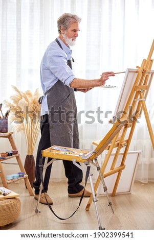 painter creating masterpiece, senior male working on canvas, using paints, paintbrushes, easel and other tools