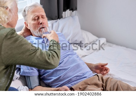 female cares her husband, give glass of water while he is suffering from disease, lying on bed at home
