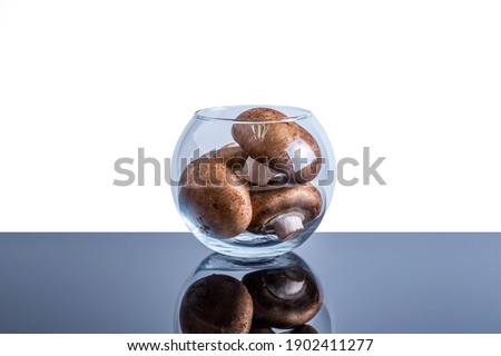 Transparent vase filled to the top with edible mushrooms on a white background with space for text