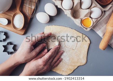 Girl prepares cookies in the shape of a heart, flat lay composition on a gray background. Cookie cutters and dough in women's hands. Concept of food for Valentine's Day, Father's Day, Mother's Day.