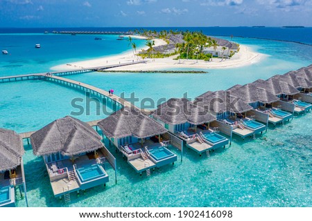Aerial view of Maldives island, luxury water villas resort and wooden pier. Beautiful sky and ocean lagoon beach background. Summer vacation holiday and travel concept. Paradise aerial landscape pano Royalty-Free Stock Photo #1902416098