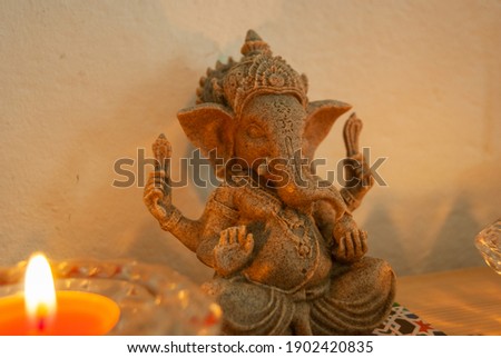 A selective focus shot of a Ganesha figurine and a lit candle on the table