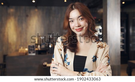 Business owner attractive young Asian woman in apron hanging we're open sign on front door  welcoming clients to new cafe. Happy waiter with protective face mask holding open sign at cafe .