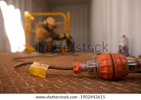 Safety workplaces approved pass test tag of electrical device attached on power cord while defocused worker using power drill on construction site 
