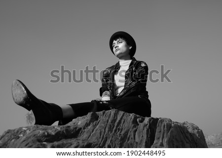 Black and white landscape of an young indian girl sitting on a rock, wearing red flower shirt and a hat 