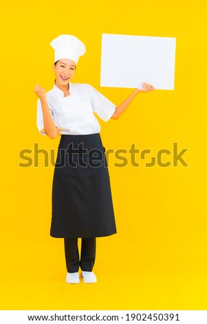 Portrait beautiful young asian chef woman with white empty billboard on yellow isolated background