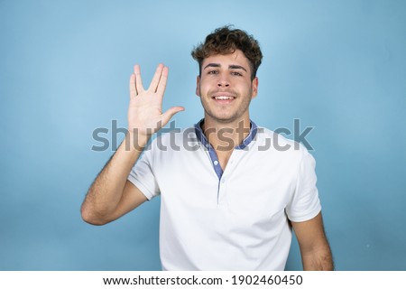 Young handsome man wearing a white t-shirt over blue background doing hand symbol
