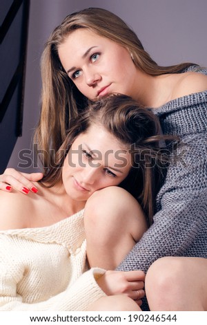 2 cute women sitting in a sweaters or jumpers on a blanket hugging each other having fun closeup portrait picture
