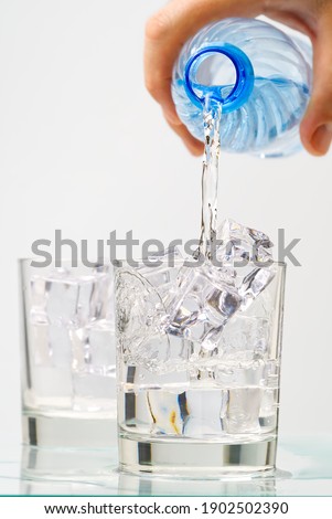 Pouring clean drinking water from blue plastic bottle into glass on blue background