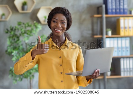 Photo portrait of african american woman holding laptop showing thumb up in modern office indoors