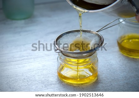 The oil is filtered into a glass jar through a metal sieve and cheesecloth. At home. Royalty-Free Stock Photo #1902513646