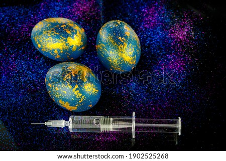 Abstract photo of eggs on galaxy glitter dark background with syringe for covid vaccination. Easter cosmic space colored eggs. World vaccination idea. Main focus on the syringe. Soft focus background