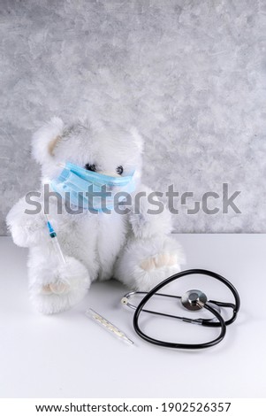 White teddy bear in a mask with a syringe. Childhood vaccination concept with copy space. 