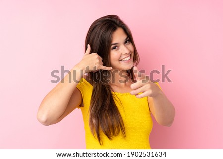 Teenager Brazilian girl over isolated pink background making phone gesture and pointing front