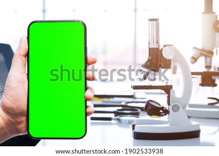 Close-up of female use Green screen smartphone blurred images with  Microscope and test tubes with lab glassware in laboratory background, research and Scientific concept