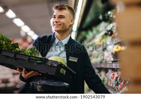 Male worker stocking up the vegetable section in supermarket. Man working in a vegetable section of a grocery store.