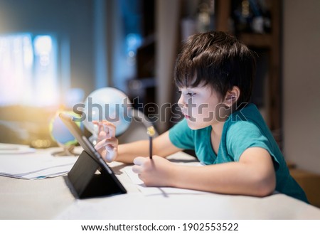 Authentic portrait kid using tablet for his homework,Child boy doing homework by using digital tablet searching information on internet,E-learning, Home schooling education concept, New normal life
