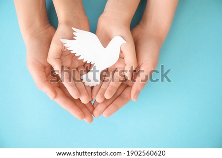 Hands of family with paper dove on color background Royalty-Free Stock Photo #1902560620