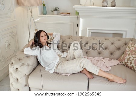Woman lies at home on the couch with headphones on and listens to music. Day off at home, relax and rest