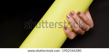 Female hand with golden nail design. Glitter gold nail polish manicure. Female hand hold yellow paper roll on black background.