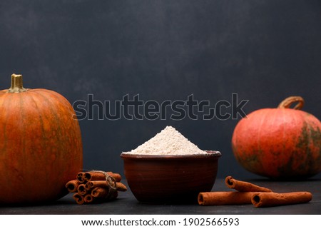 Orange pumpkins, cinnamon sticks, flour in bowl on black table against blue wall background. Autumn menu or fall homemade cooking concept. Home kitchen, thanksgiving, closeup, side view, copy space
