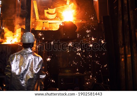 Foundry worker controlling iron melting in furnace. Sparks flying around. Royalty-Free Stock Photo #1902581443