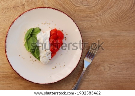 Heart shaped Italian Caprese Salad arranged by Italian basil,buffalo mozzarella and tomatoes look like Italian Flag on plate with wooden table background.Love Italian food concept for Valentine day  Royalty-Free Stock Photo #1902583462